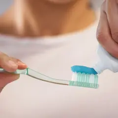 Nakładanie niebieskiej pasty do zębów z fluorkiem cyny na szczoteczkę.