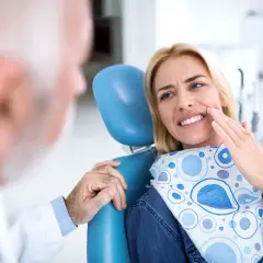 Pacjentka u dentysty wskazuje na ból zęba, który może być objawem zapalenia tkanek okołowierzchołkowych.