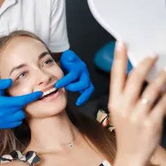 Uśmiechnięta pacjentka ocenia efekt odbudowy szkliwa u dentysty, trzymając lusterko.