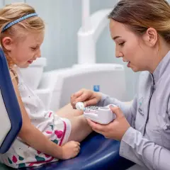 Dentystka pokazuje dziecku model szczęki, tłumacząc jak używać pasty z chlorkiem cetylopirydyniowym do higieny jamy ustnej.