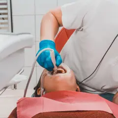Dentysta w niebieskich rękawiczkach wykonuje piaskowanie zębów pacjentowi, używając specjalistycznego sprzętu.