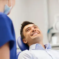 Uśmiechnięty mężczyzna w gabinecie dentystycznym, rozmawiający z higienistką. Pytanie o fluoryzacja zębów skutki uboczne.