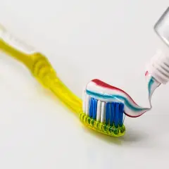 Żółta szczoteczka z kolorową pastą do zębów, zawierającą fluorek sodu, który chroni przed próchnicą. Fluor w paście wzmacnia szkliwo.