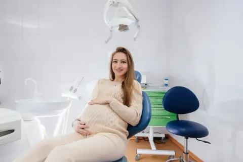 Uśmiechnięta ciężarna kobieta w gabinecie stomatologicznym. Odpowiedź na pytanie: czy można leczyć zęby w ciąży.