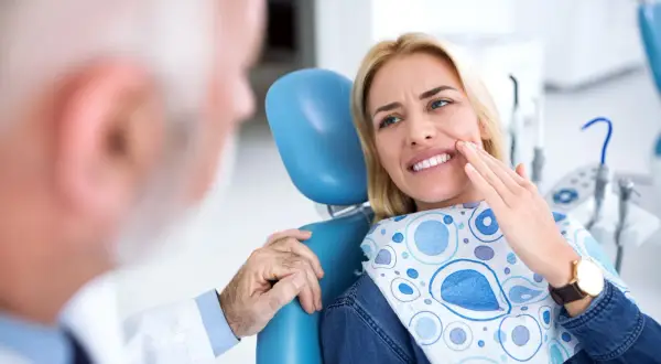 Pacjentka u dentysty wskazuje na ból zęba, który może być objawem zapalenia tkanek okołowierzchołkowych.