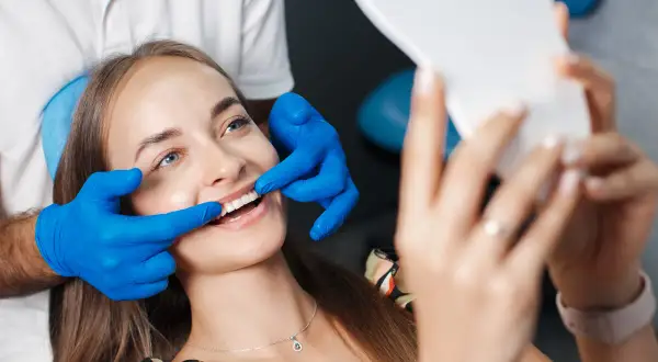 Uśmiechnięta pacjentka ocenia efekt odbudowy szkliwa u dentysty, trzymając lusterko.
