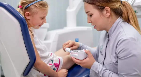 Dentystka pokazuje dziecku model szczęki, tłumacząc jak używać pasty z chlorkiem cetylopirydyniowym do higieny jamy ustnej.