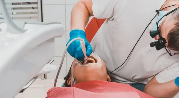 Dentysta w niebieskich rękawiczkach wykonuje piaskowanie zębów pacjentowi, używając specjalistycznego sprzętu.