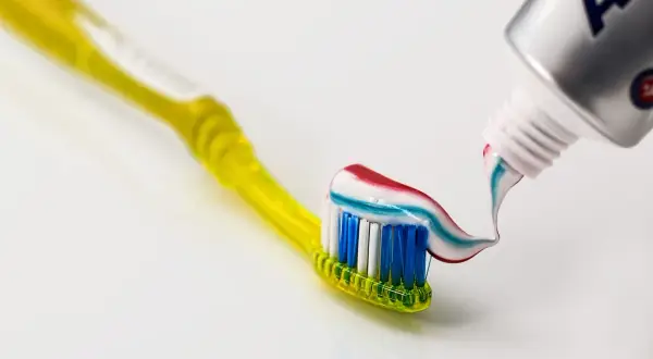 Żółta szczoteczka z kolorową pastą do zębów, zawierającą fluorek sodu, który chroni przed próchnicą. Fluor w paście wzmacnia szkliwo.