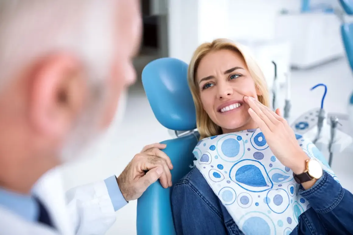 Pacjentka u dentysty wskazuje na ból zęba, który może być objawem zapalenia tkanek okołowierzchołkowych.
