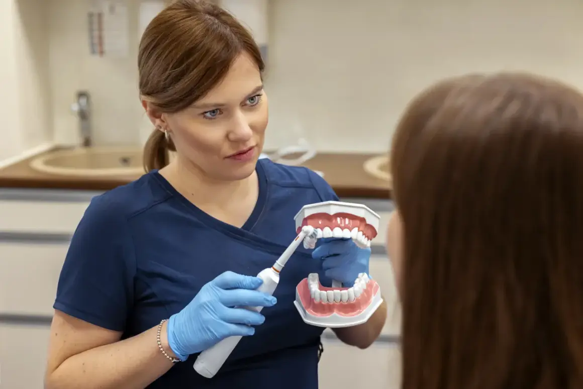 Dentystka pokazuje pacjentowi, jak prawidłowo myć zęby za pomocą modelu szczęki i szczoteczki elektrycznej.