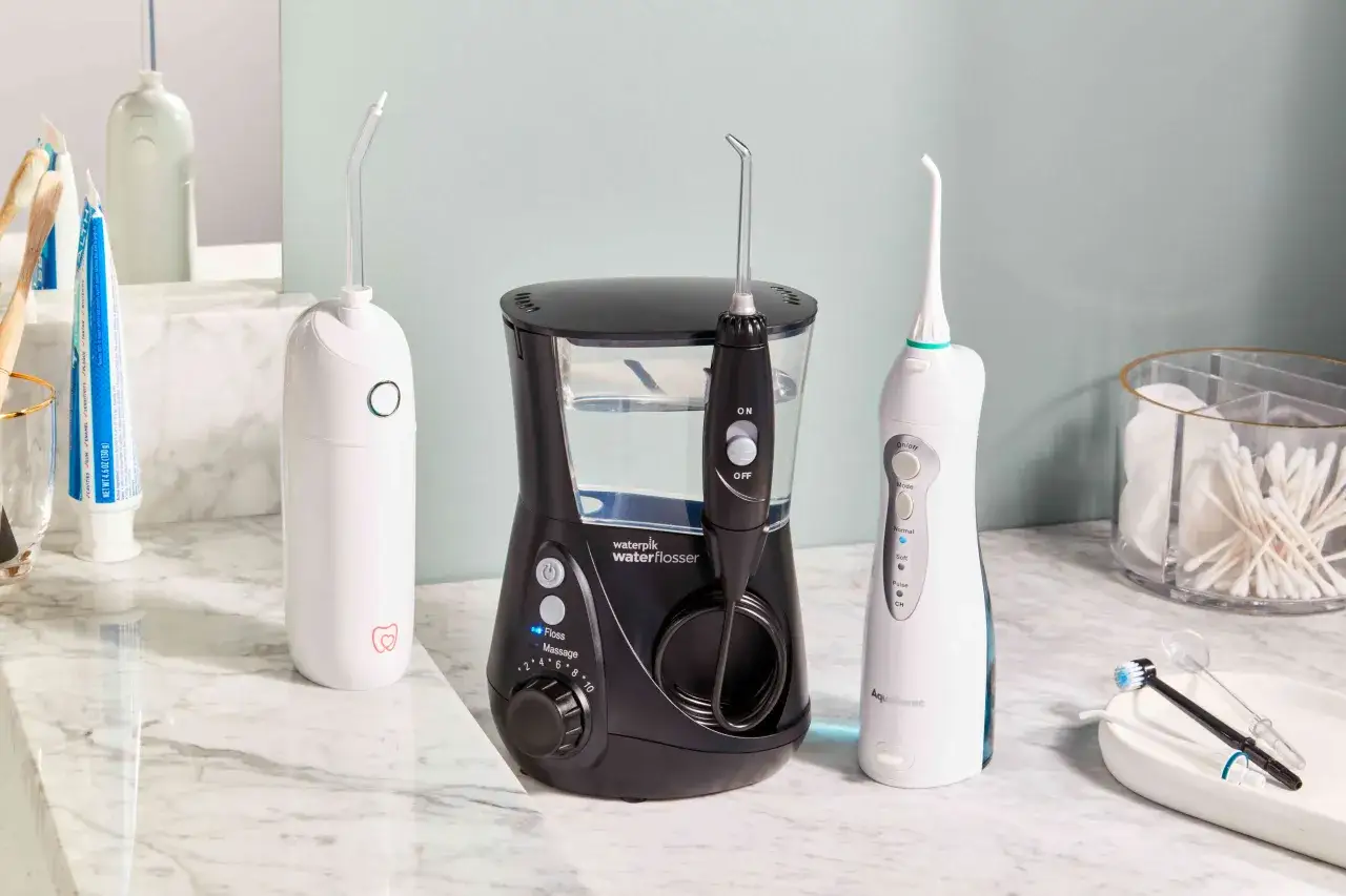Jaki irygator wybrać? Na blacie łazienkowej stoją trzy irygatory: biały, czarny Waterpik i biało-niebieski Aquasonic.