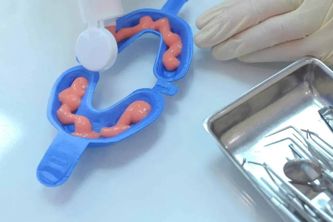 Niebieska łyżka z różową pastą do fluoryzacji, obok tacka z narzędziami dentystycznymi. Czy fluoryzacja w szkole tak czy nie?