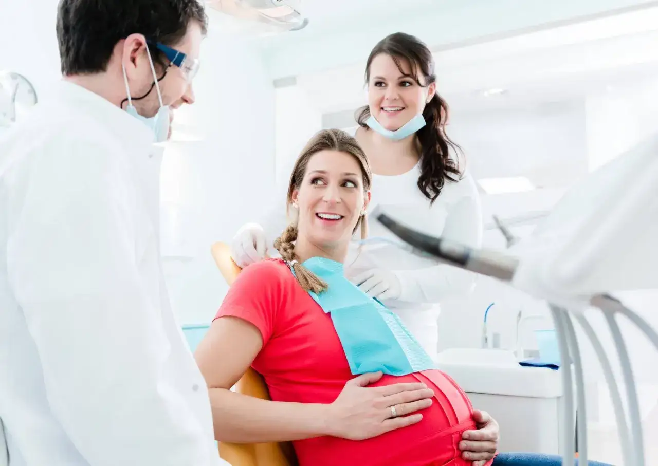 Dentysta i asystentka uśmiechają się do ciężarnej pacjentki. Odpowiedź na pytanie: czy można leczyć zęby w ciąży jest pozytywna.