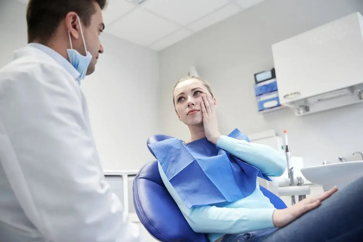 Pacjentka w gabinecie dentystycznym skarży się na ból, wskazując na objawy przeciążenia zęba.