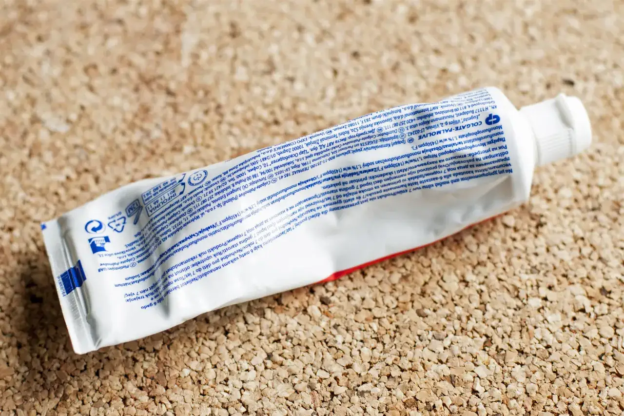 Biała tubka pasty do zębów Colgate-Palmolive leży na korkowym tle. Widoczne są różne kolory na pastach do zębów, choć głównie biały.