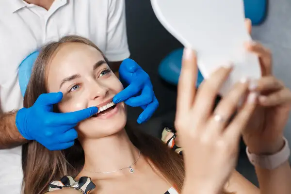Uśmiechnięta pacjentka ocenia efekt odbudowy szkliwa u dentysty, trzymając lusterko.