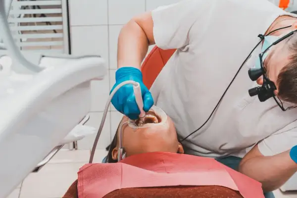 Dentysta w niebieskich rękawiczkach wykonuje piaskowanie zębów pacjentowi, używając specjalistycznego sprzętu.