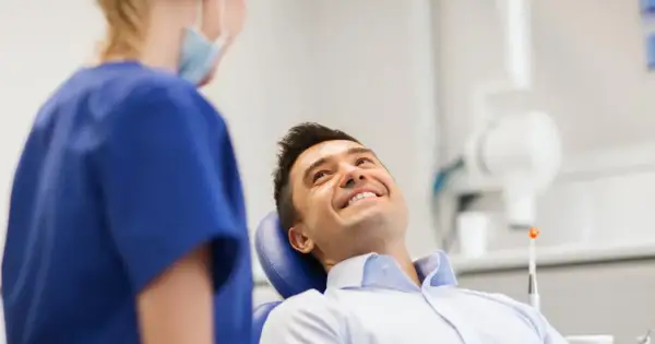 Uśmiechnięty mężczyzna w gabinecie dentystycznym, rozmawiający z higienistką. Pytanie o fluoryzacja zębów skutki uboczne.